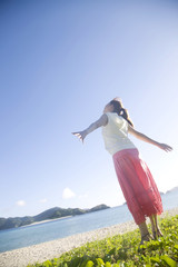 海辺で両手を広げ太陽の光を浴びる女性の後姿