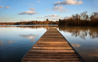 Landscape of fishing jetty on calm lake at sunset with reflectio