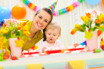 Fototapeta premium Smiling mom and eat smeared baby on birthday celebration party