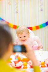 Mother making photos of happy baby on first birthday party
