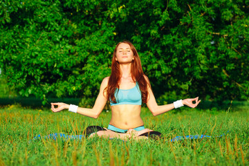 Naklejka na ściany i meble Young woman doing yoga exercise on green park