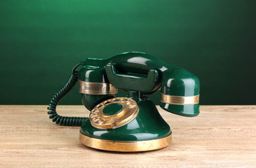 Retro phone on wooden table on green background
