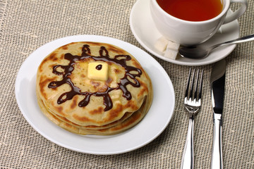Pancakes on a plate and a cup of tea with tableware