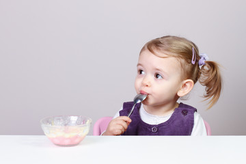 Adorable little girl eating creamy pudding with spoon