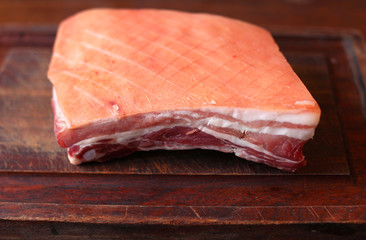 Pork belly with scored skin, uncooked on a wooden cutting board