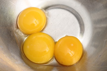 Three yellow egg yolks in a metallic bowl for cooking