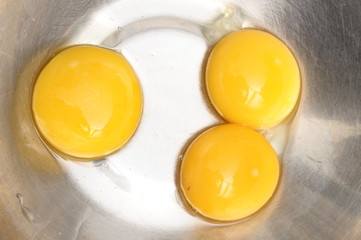 Three yellow egg yolks in a metallic bowl for cooking