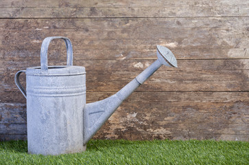 watering can on grass against a wooden wall