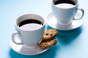 Two coffee cups with cookies on blue background