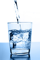 water pouring in to glass with ice cubes on glossy background