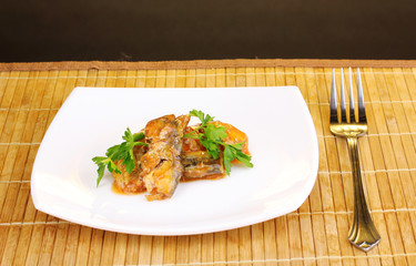 Tasty sardines on plate on wooden mat on brown background