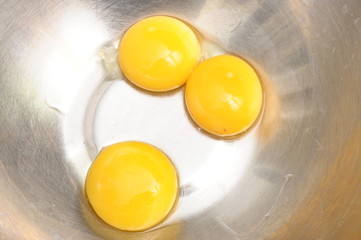 Three yellow egg yolks in a metallic bowl for cooking