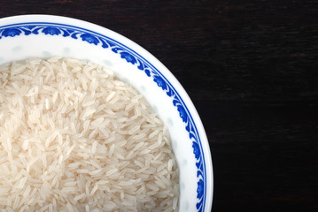 bowl of uncooked white rice on wooden background.