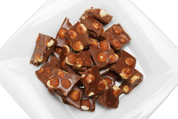 broken chocolate pieces with nuts on white plate, isolated