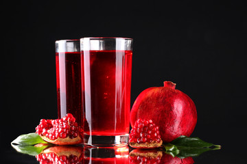 ripe pomergranate and glasses of juice on black background