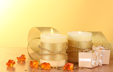 Beautiful candles and gifts on wooden table on yellow background