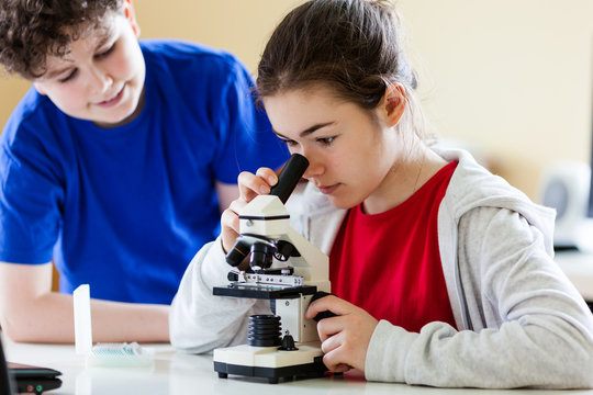 Girl and boy examining preparation under the microscope - Powered by Adobe