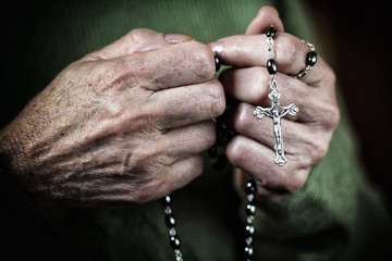  elderly woman's hands tighten a classic Christian rosary for prayer. concept of religious belief...