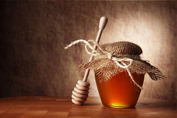 Pot of honey and wooden stick are on a table. - obrazy, fototapety, plakaty