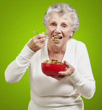 Senior Woman Eating Cereals Out Of A Red Bowl Against A Green Ba