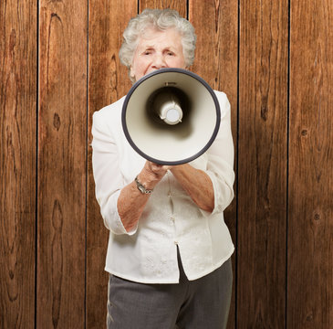 portrait of senior woman screaming with megaphone against a wood