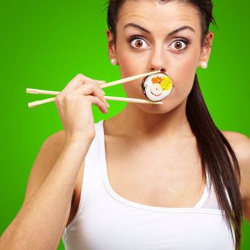 young woman covering her mouth with a sushi piece against a gree