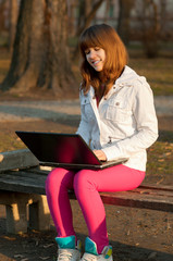 Pretty teenage girl typing on notebook in the park