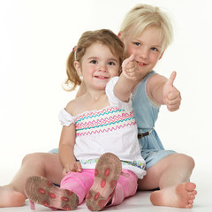Cute little girls sitting on the floor and show thumbs up