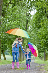 mother and her daughter with umbrellas in spring alley