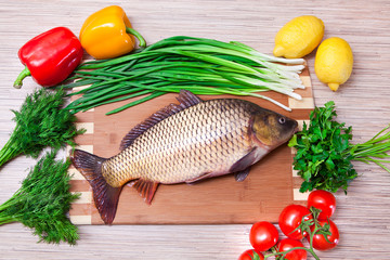 Fresh fish on a kitchen board with vegetables.