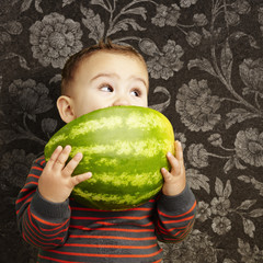 Fototapeta premium portrait of a handsome kid holding watermelon and sucking agains