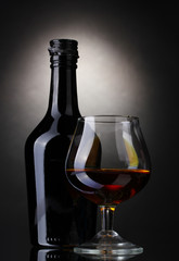 Glass of brandy and bottle on gray background