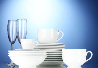 Obraz na płótnie Canvas empty bowls, plates, cups and glasses on blue background