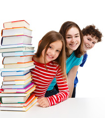 Students peeking behind pile of books on white