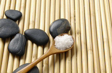 sea salt in a wooden spoon with Stones on bamboo stick straw mat