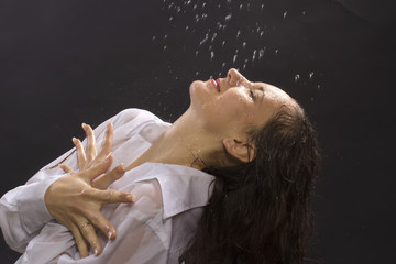 The young woman under water drops on a black background