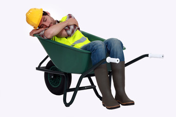 A road worker sleeping in a wheelbarrow.