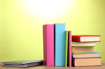 Books with stationery on wooden table on green background