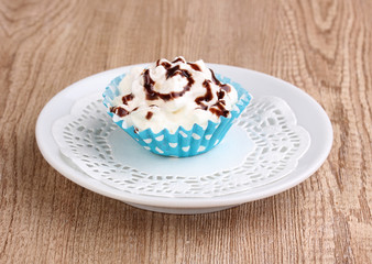 Creamy cupcake on saucer on wooden background