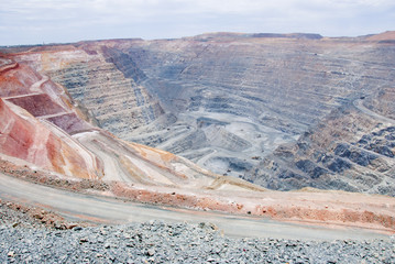 Big mine pit with little dump trucks and reddish soil