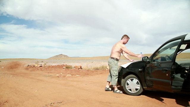 Young man looking at a map on the car hood