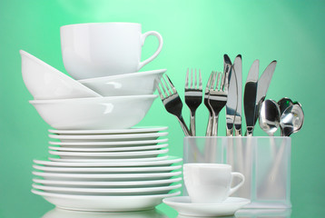 Fototapeta na wymiar Clean plates, cups and cutlery on green background