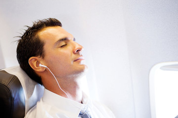 tired businessman listening music and relaxing on airplane