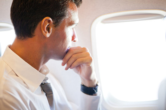 Thoughtful Businessman On Airplane Looking Outside