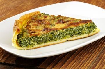 Slice of spinach tart with parmesan - wooden background