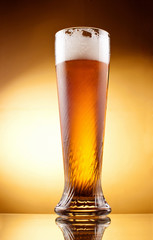 Frosty glass of light beer with froth over yellow background