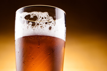 Glass of beer with froth close up on a yellow background