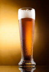 Frosty glass of light beer with froth over yellow background