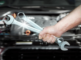 Close up of a hand with tools in front of an engine bay