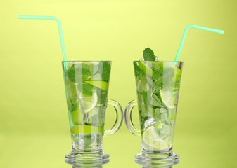 Glasses of cocktail with lime and mint on green background